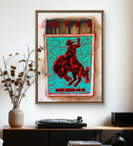 A framed art print featuring a vibrant turquoise background with a red cowboy riding a bucking horse, styled on a white wall above a modern media console with a turntable and decorative vases.
